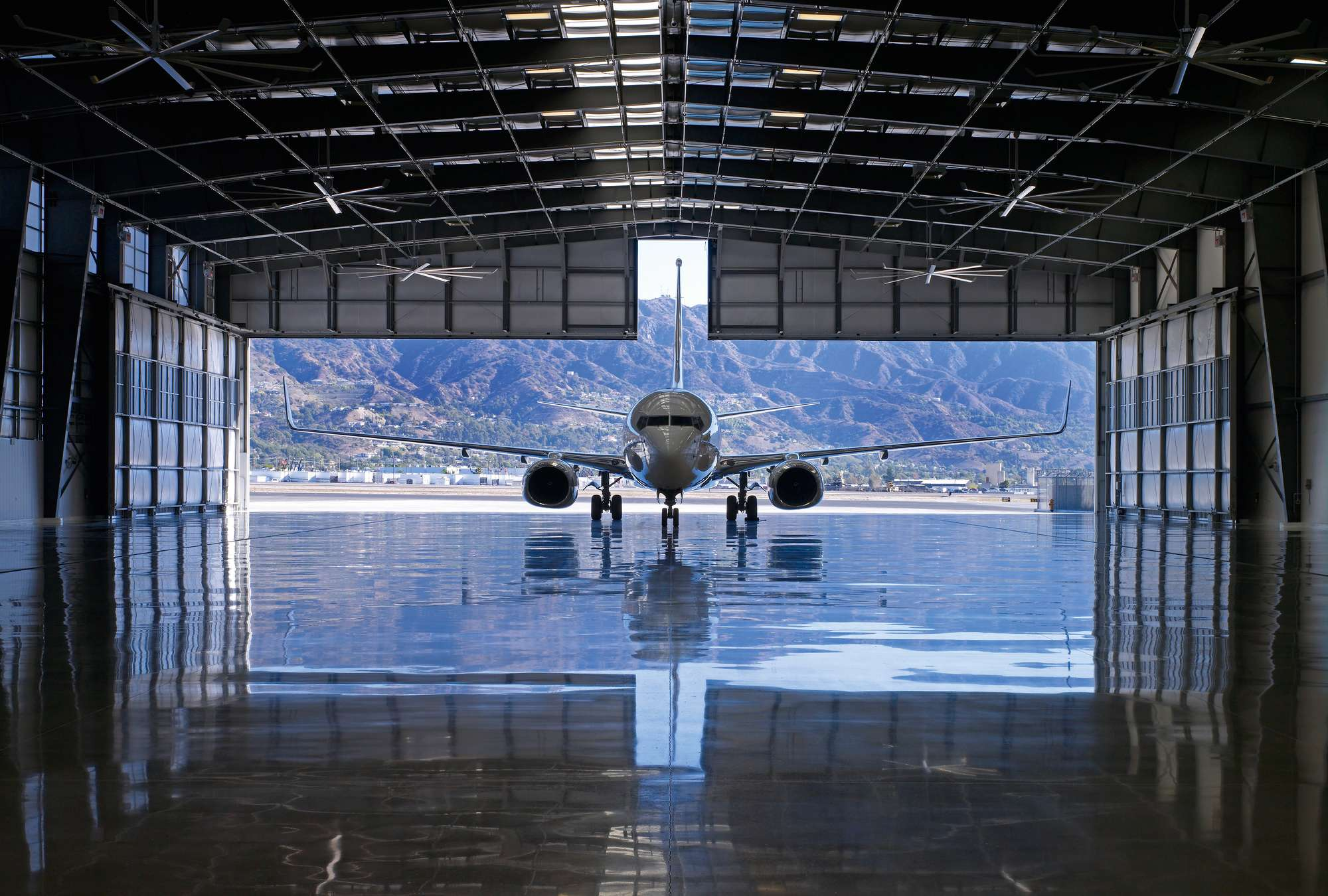 Private jet parked inside a modern aircraft hangar with mountains visible through the open hangar doors