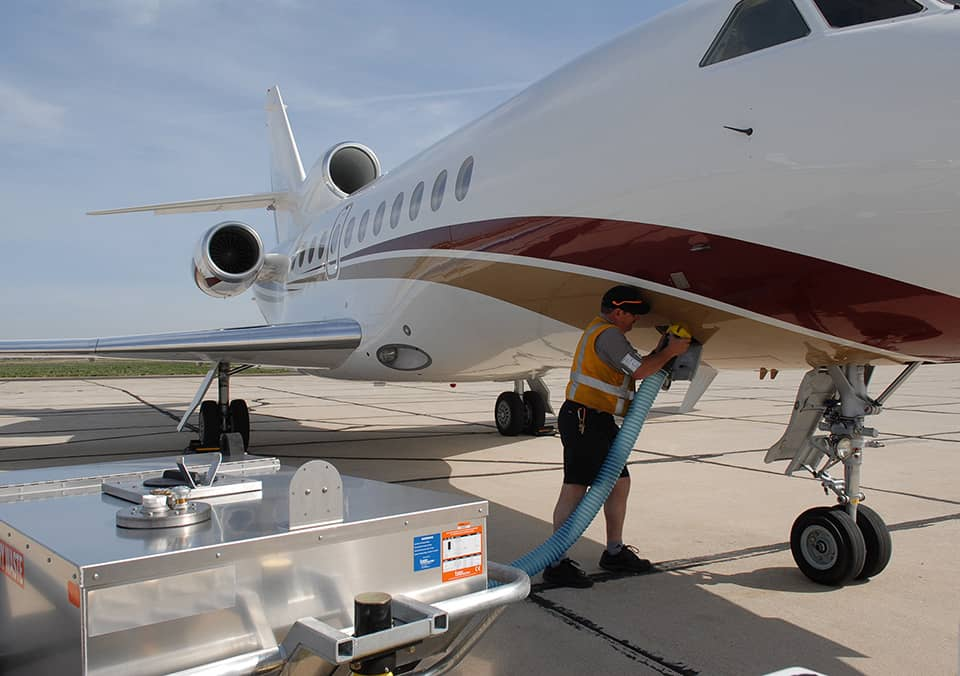 Ground crew technician servicing a private jet lavatory with drain hose connected to a lavatory service cart