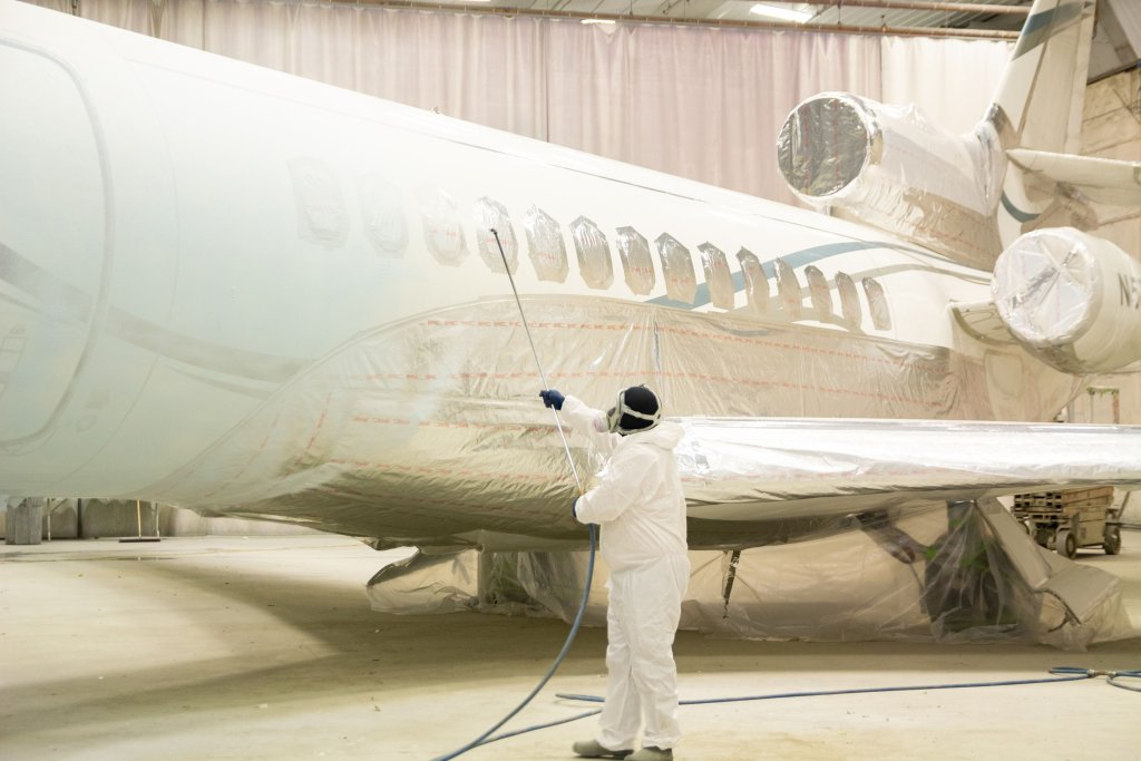 Technician in protective suit spray painting a commercial aircraft in a hangar